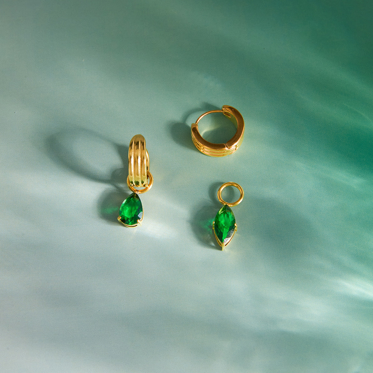 Close-up of Noor green huggie earrings — 18k gold-plated teardrop crystal huggies for statement evening wear.